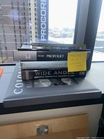 Stack of six photography books shown including National Geographic Wide Angle, Stunning Photographs, two copies of A Guide to Colorado's Best Photography Locations, Itoya Profolio, and Colorado Black on White.
