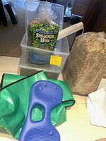 Plastic pots, sphagnum moss packs, green potting soil carrier, blue kneeling pad, and white cloth pieces arranged on floor
