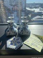 Four Royal Copenhagen Blue Fluted Lace porcelain candlesticks arranged on a flat surface in daylight, showing blue floral designs and lace edges, alongside a handwritten note describing the item.