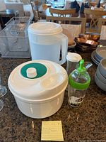 Photo showing the white plastic salad spinner, white pitcher, glass dressing bottles on countertop