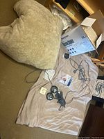 Photo showing the Sunbeam blanket khaki color folded on the floor with two black round controllers with cables and the Westinghouse blanket box on tan carpet.