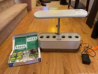 Front view of AeroGarden unit showing LED light panel and planter holes with garden supplies box to the side.