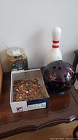 Photo showing bowling ball coin bank, bowling pin coin bank, jar of coin wrappers, and box of pennies on wooden surface