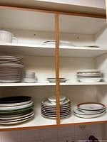 Photo showing multiple stacks of plates, bowls, and platters arranged on shelves with white backing.