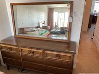 Frontal view of the wooden dresser with attached large mirror, showing all nine drawers and mirror reflection of bedroom.