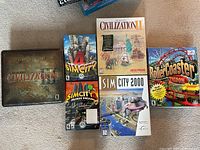 Full lot overview photo showing six boxed PC game titles from the Civilization, SimCity and RollerCoaster Tycoon series arranged on carpet.
