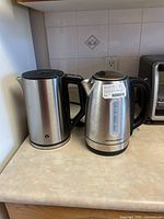 Photo showing both kettles side by side on countertop, stainless steel finish with black handles