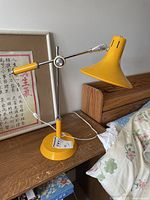 Full view of yellow metal table lamp on wooden surface showing adjustable arm and conical lampshade.