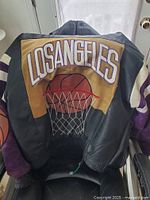 Back view of black leather varsity jacket with yellow panel and embroidered 'Los Angeles' text above basketball hoop graphic