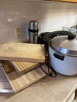 Rice cooker and roaster with thermos and wooden cutting boards and trays in the background