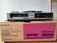 Front view of Sony Betamax SL-2401 player with original box behind showing product details and dimensions.