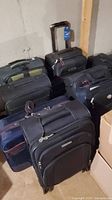 Photo shows the seven suitcases arranged in basement with visible handles and wheels for several items.