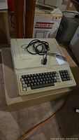 Front three-quarter view of beige microcomputer with built-in keyboard and attached power cable
