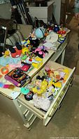 Overview of a metal desk with a variety of vintage children's toys and games placed on top and in an open drawer. Toys include plush animals, figures, and boxed games, arranged on and inside the desk.