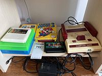 Photo showing the full set of console, NES adapter, and various game cartridges including Super Mario Bros 3 and Micro Genius games stacked on boxes.