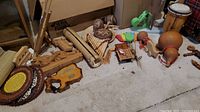 Wide view of instruments and decor showing pan flute, carved wooden violin, xylophone, maracas, drums, and carved wooden pieces arranged on carpeted floor