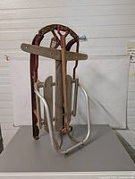 Front view of antique wooden sled showing wooden slats, metal frame, and red leather straps.