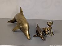 Large and small brass dolphin figurines with brass cat figurine in background.