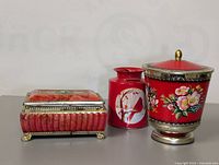 Front angle showing three decorative canisters: a floral tin canister, a red ceramic canister with bird design, and a decorative glass hinged canister.