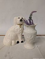 Photo of white ceramic dog figurine and white ceramic vase with artificial lavender sprigs