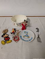 Photo displaying seven vintage Mickey Mouse themed items on a light-colored surface, featuring ceramics, figurines, a keychain, and a fork.