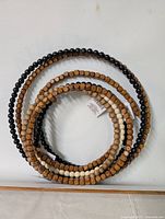 Photo of five wooden bead rings hanging on a white wall, displaying different shades of wood and one black bead ring.