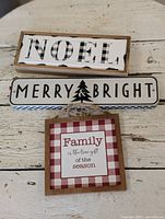 Three holiday-themed signs: NOEL, MERRY & BRIGHT, and Family holiday phrase