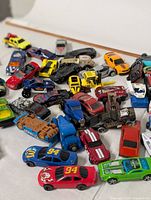 Photo showing a spread of old toy cars including racing cars with numbers, a brown vintage van, and various colored vehicles.