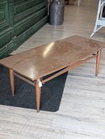Full view of rectangular mid century modern wooden coffee table on light wood floor with black rug underneath.
