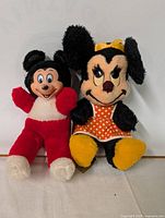Photo showing Mickey (red and white) and Minnie (black with orange polka dot dress) plush toys together
