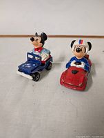 Front view of two Mickey Mouse toy cars: blue jeep and red race car.