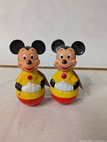 Photo shows two vintage plastic roly-poly toys modeled after Disney's Mickey Mouse characters, painted in yellow, red, black, and white colors.