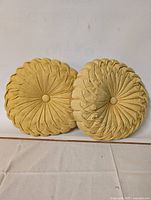 Two vintage round mustard yellow pillows side by side, showing different pleated and ruched fabric patterns with button centers.