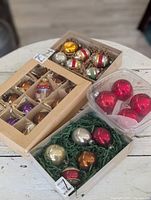 Photo showing multiple boxes of vintage Christmas ornaments including striped silver ones, assorted colorful ones, loose red ornaments, and a box with silver, red, and orange spheres.