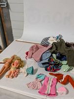 Two vintage dolls, one small blond and one articulated, with a pile of handmade vintage Barbie doll clothes in various styles and colors.