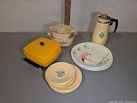 Photo of vintage kids dishes including yellow square pot, beige pot, beige carafe, three small plates, and flamingo plate.