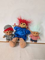 Three troll dolls photographed against a plain white background. The trolls have colorful hair and distinctive clothing.