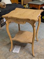 Front angled view of a wooden accent table showing its detailed carved edges, curved legs, and lower shelf.