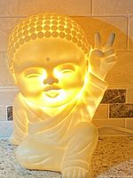 Front illuminated view of Buddha lamp glowing warmly on counter with peace sign gesture.