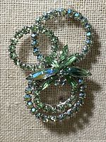 Front view of Sherman vintage brooch showing three silver-tone circular loops with green Swarovski crystals and leaf accent crystals.
