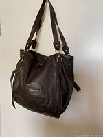 Front and side views of black genuine leather Valentina shoulder bag showing brand logo, straps, buckles and leather tassel accents.