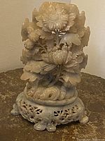 Front view of vintage Asian hand-carved floral stone sculpture showing detailed flower and leaf carvings with pierced base on a table surface.