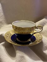 Photo of the teacup stacked inside the saucer showing the gold chintz pattern, cobalt blue, and pale yellow accents with gold trim.