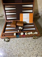 Opened backgammon set showing board, leather dice cups, checkers, dice, and rules booklet.