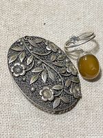 Close-up of vintage silver floral filigree brooch and silver ring with amber cabochon showing details and texture
