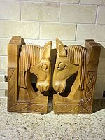 Front view of two wooden horse head bookends facing each other on a countertop with tile backsplash