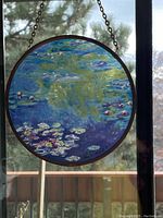 Full view of the round stained glass sun catcher hanging against a window, depicting Claude Monet's Water Lilies.