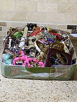 Overview of box filled with assorted vintage jewellery showcasing a variety of bracelets, necklaces, and earrings in multiple colors and materials.