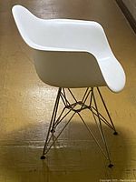 Side view of white molded plastic arm chair with chrome Eiffel-style legs on a yellow floor.