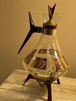 Full view of the glass coffee carafe with handle and stand on a stone surface against beige background